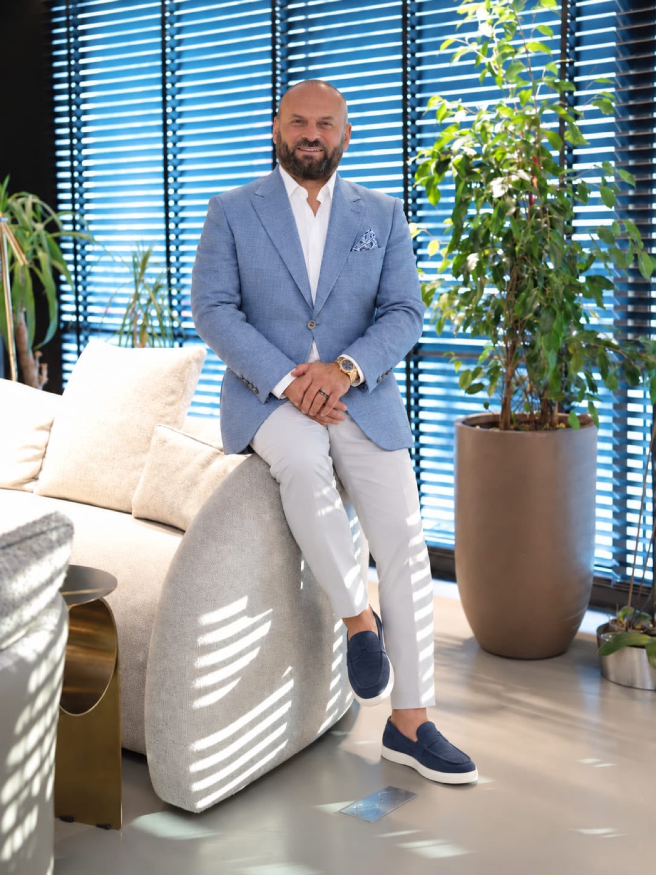 Bülent Alıcı, mavi takım elbise ile koltukta.